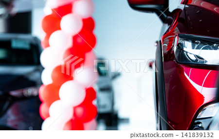 Modern red SUV displayed in car showroom with illuminated LED headlight and promotional balloons, premium automobile dealership interior for vehicle sales, automotive marketing and transportation. Modern red SUV displayed in car showroom with illuminated LED headlight and promotional balloons, premium automobile dealership interior for vehicle sales, automotive marketing and transportation. 141839132