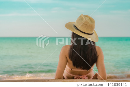 Rear view of woman wearing a straw hat looking at the turquoise tropical ocean, peaceful summer vacation, luxury beach resort, wellness travel destination and relaxation concept. Tourism promotion. Rear view of woman wearing a straw hat looking at the turquoise tropical ocean, peaceful summer vacation, luxury beach resort, wellness travel destination and relaxation concept. Tourism promotion. 141839141