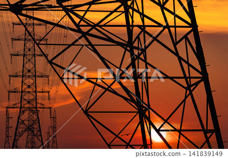 Silhouette of high voltage electricity transmission towers and power lines against a glowing sunset sky. Electrical infrastructure, utility network, energy supply, sustainable engineering, smart grid. Silhouette of high voltage electricity transmission towers and power lines against a glowing sunset sky. Electrical infrastructure, utility network, energy supply, sustainable engineering, smart grid. 141839149