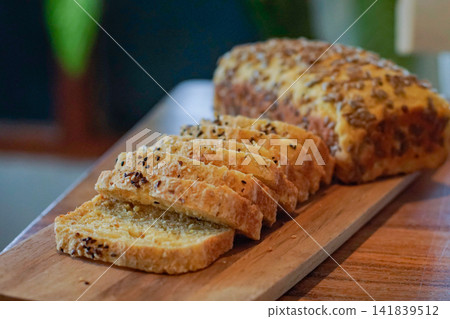 Fresh sliced seeded bread arranged on a rustic wooden board with a whole loaf in the background, featuring mixed seeds, golden crust and a warm natural homemade bakery setting. Fresh sliced seeded bread arranged on a rustic wooden board with a whole loaf in the background, featuring mixed seeds, golden crust and a warm natural homemade bakery setting. 141839512
