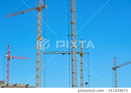 Construction crane stands tall against the blue sky during the day in an urban area Construction crane stands tall against the blue sky during the day in an urban area 141839675