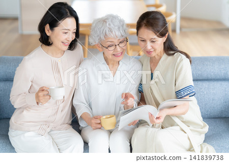 一位老婦人和她的朋友正在客廳看雜誌。 141839738