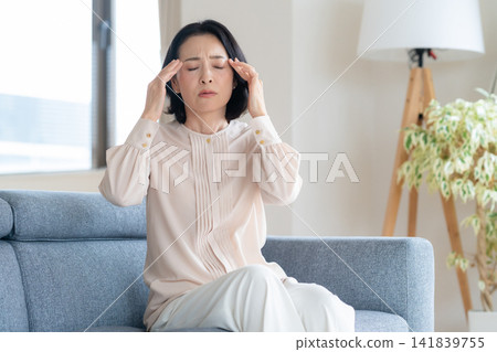 A middle-aged woman who is feeling unwell in the living room A middle-aged woman who is feeling unwell in the living room 141839755