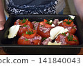 Close up of a woman's hands holding a dish containing homemade stuffed tomatoes ready to be placed in the oven, showing a traditional cooking preparation. 141840043