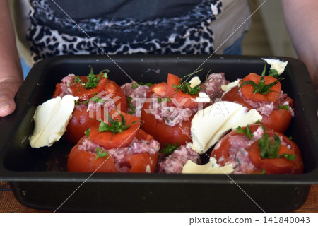 Close up of a woman's hands holding a dish containing homemade stuffed tomatoes ready to be placed in the oven, showing a traditional cooking preparation. Close up of a woman's hands holding a dish containing homemade stuffed tomatoes ready to be placed in the oven, showing a traditional cooking preparation. 141840043