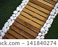 Detail of a garden pathway featuring artificial grass, wooden decking tiles and white pebbles along the border, creating a modern outdoor landscaping design. 141840274