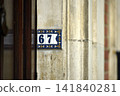Close up of a decorative enamel house number 67 displayed on the entrance of a traditional beige stone house, highlighting an architectural detail with French character. 141840281
