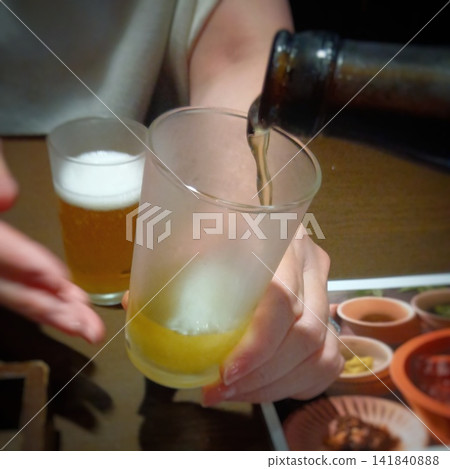 一瓶冰啤酒被倒入杯中,展現了晚上在居酒屋(日本酒吧)喝酒的場景。 一瓶冰啤酒被倒入杯中,展現了晚上在居酒屋(日本酒吧)喝酒的場景。 141840888
