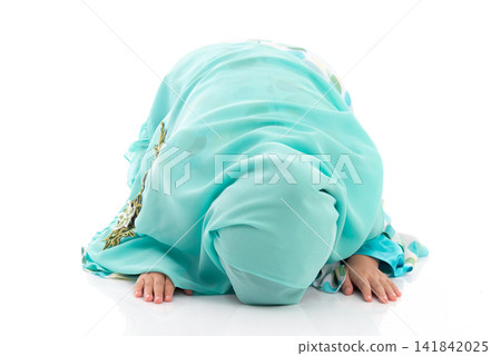 Charming young Asian Muslim child in traditional headscarf bowing down in prayer during holy month Ramadan. Charming young Asian Muslim child in traditional headscarf bowing down in prayer during holy month Ramadan. 141842025