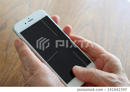 特寫鏡頭:一位老婦人坐在桌前,雙手拿著一支智慧型手機。 特寫鏡頭:一位老婦人坐在桌前,雙手拿著一支智慧型手機。 141842397