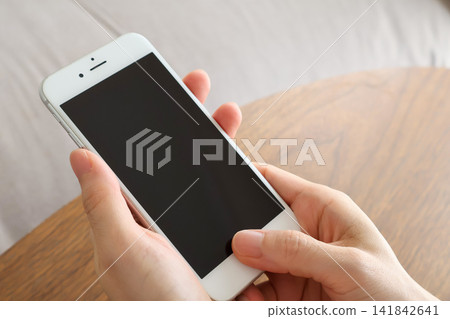 A woman's hand holding a smartphone on a wooden table A woman's hand holding a smartphone on a wooden table 141842641