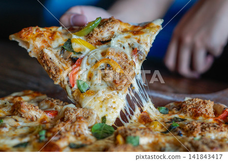 Cheesy Pizza Slice with Fried Chicken Being Lifted, Close Up of Melting Mozzarella and Toppings for Fast Food and Delivery Meal Concepts Cheesy Pizza Slice with Fried Chicken Being Lifted, Close Up of Melting Mozzarella and Toppings for Fast Food and Delivery Meal Concepts 141843417