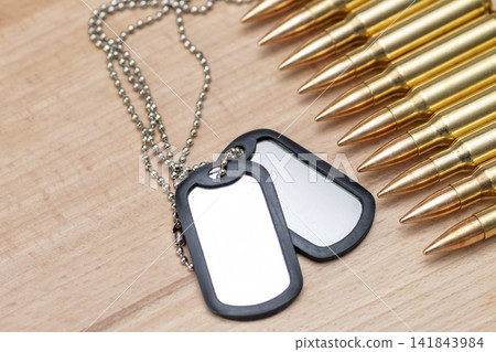 Blank military dog tags beside rifle cartridges on wooden surface Blank military dog tags beside rifle cartridges on wooden surface 141843984