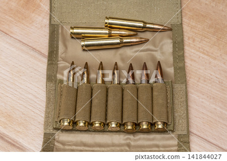 Rifle cartridges arranged in open tactical pouch on light wooden surface Rifle cartridges arranged in open tactical pouch on light wooden surface 141844027