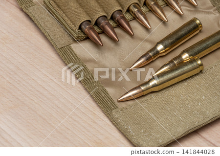 Rifle cartridges arranged in tan ammo pouch on wooden surface Rifle cartridges arranged in tan ammo pouch on wooden surface 141844028