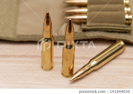 Close up rifle cartridges standing beside ammunition pouch on wooden surface Close up rifle cartridges standing beside ammunition pouch on wooden surface 141844030