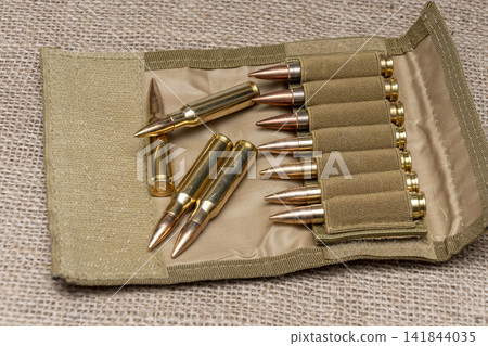 Open tan ammunition pouch with rifle cartridges arranged on burlap Open tan ammunition pouch with rifle cartridges arranged on burlap 141844035