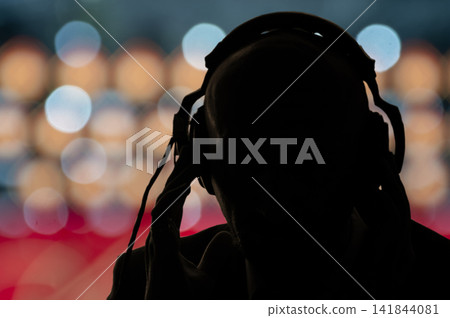 The dark silhouette of a man in headphones on the background of multicolored glare and lights of the city. Concept: government surveillance of people, secret special agent eavesdropping on The dark silhouette of a man in headphones on the background of multicolored glare and lights of the city. Concept: government surveillance of people, secret special agent eavesdropping on 141844081