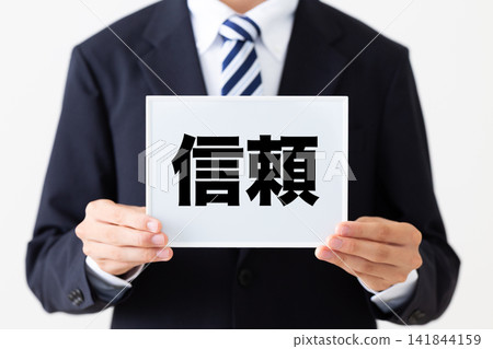 一位身著西裝的年輕商人,手持一塊結實的白板。 一位身著西裝的年輕商人,手持一塊結實的白板。 141844159