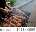 Chef hands turning juicy pork shashlik skewers over glowing charcoal embers on outdoor metal mangal grill preparing traditional barbecue meal 141844695