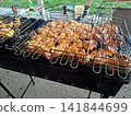 Delicious chicken meat cooking in wire grate mesh over hot barbecue grill charcoal embers for summer picnic outdoor dinner party food preparation 141844699