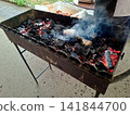Smoke rising from hot burning charcoal embers in outdoor barbecue metal grill preparing heat for summer picnic food roasting and outdoor cooking 141844700