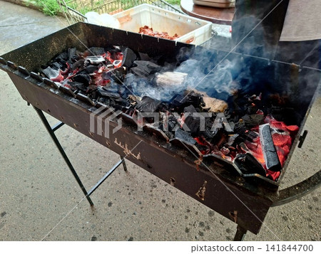 Smoke rising from hot burning charcoal embers in outdoor barbecue metal grill preparing heat for summer picnic food roasting and outdoor cooking Smoke rising from hot burning charcoal embers in outdoor barbecue metal grill preparing heat for summer picnic food roasting and outdoor cooking 141844700