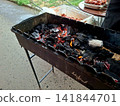 Side angle view of outdoor metal barbecue mangal filled with glowing charcoal embers ready for grilling meat during summer picnic family gathering 141844701