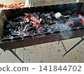 Close up of burning charcoal embers with smoke rising from metal barbecue grill prepared for outdoor picnic cooking and summer food grilling party 141844702