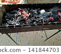 Hot glowing charcoal embers burning with red heat inside outdoor metal mangal grill for picnic barbecue cooking and summertime grilling food preparation 141844703