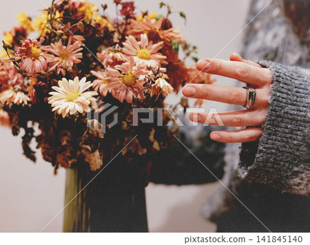 Woman's hand touching a colorful autumn chrysanthemum bouquet at home, capturing a mindful floral moment with warm seasonal tones, slow living, botanical beauty and creative lifestyle inspiration art. Woman's hand touching a colorful autumn chrysanthemum bouquet at home, capturing a mindful floral moment with warm seasonal tones, slow living, botanical beauty and creative lifestyle inspiration art. 141845140