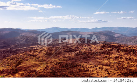 A vast panorama captures rolling mountains, rocky hills, and sparse valleys under a partly cloudy sky. A vast panorama captures rolling mountains, rocky hills, and sparse valleys under a partly cloudy sky. 141845283
