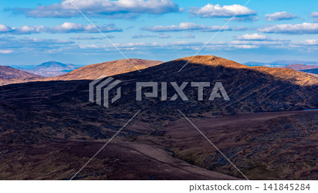The wide-angle photograph displays a sequence of mountain chains receding into the distance under a bright sky. The wide-angle photograph displays a sequence of mountain chains receding into the distance under a bright sky. 141845284