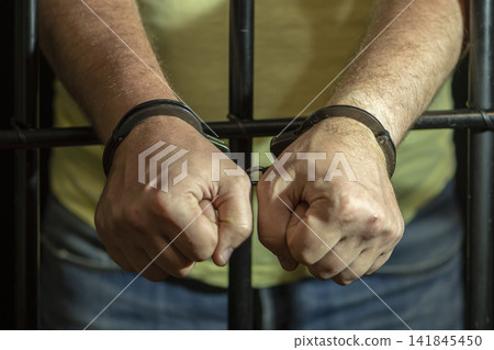 A man in jeans handcuffed behind bars is a symbol of imprisonment. 141845450