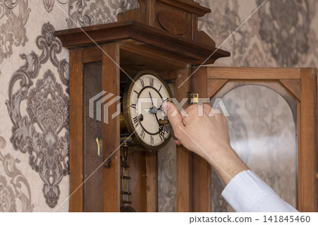 Time Transition: A man moves the hands on a classic pendulum clock, conveying the atmosphere of cosiness and old-fashioned everyday life. Time Transition: A man moves the hands on a classic pendulum clock, conveying the atmosphere of cosiness and old-fashioned everyday life. 141845460