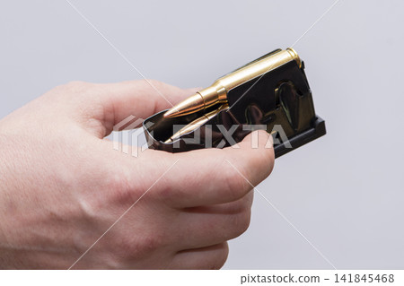 A male hunter loads cartridges for a rifle magazine on a light background, equip a combat weapon. A male hunter loads cartridges for a rifle magazine on a light background, equip a combat weapon. 141845468