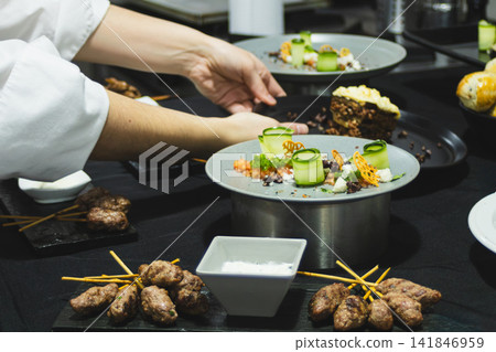 Chef arranging beautifully plated gourmet dishes, featuring artfully presented vegetables, savory meat skewers, and a diverse range of flavors and textures for a culinary event Chef arranging beautifully plated gourmet dishes, featuring artfully presented vegetables, savory meat skewers, and a diverse range of flavors and textures for a culinary event 141846959