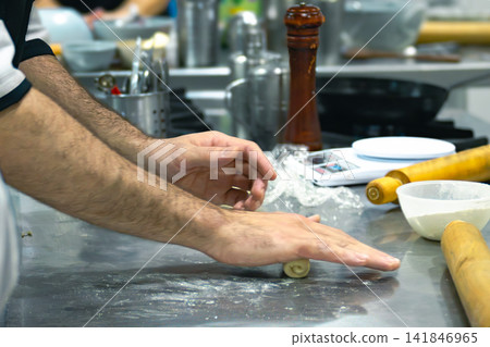 Chef hands expertly rolling a small piece of dough on a metal kitchen counter dusted with flour, showcasing dedication to cooking and the culinary arts Chef hands expertly rolling a small piece of dough on a metal kitchen counter dusted with flour, showcasing dedication to cooking and the culinary arts 141846965