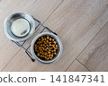 A bowl with dry dog kibble food and water on the wood floor. Snack for dogs. 141847341