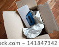 Person unpack the cardboard box with new mobile phone on the wood table. Smartphone on the wood table. 141847342