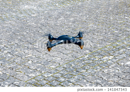 Black drone waiting on the stone road. Innovative modern technology. Black drone waiting on the stone road. Innovative modern technology. 141847343