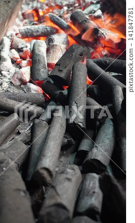 Glowing red hot charcoal pieces burning in a grill at a street food stall, cooking energy fuel and power concept Glowing red hot charcoal pieces burning in a grill at a street food stall, cooking energy fuel and power concept 141847781