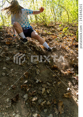 Active young woman sliding down a steep dirt slope covered in dry leaves Active young woman sliding down a steep dirt slope covered in dry leaves 141848201