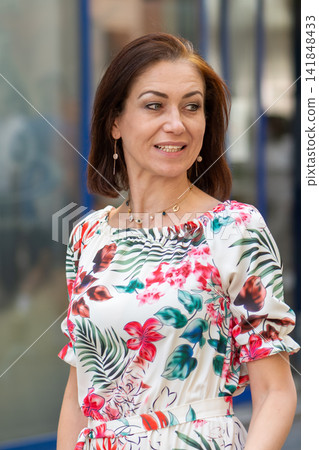 Smiling elegant woman in floral dress looking away during outdoor portrait Smiling elegant woman in floral dress looking away during outdoor portrait 141848433