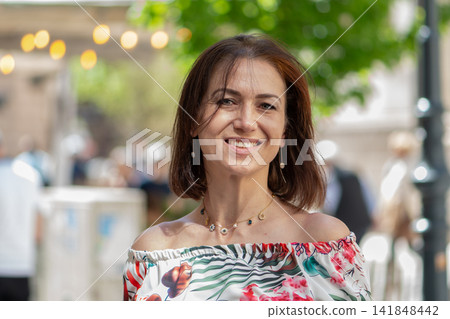 Smiling middle aged woman in floral off shoulder blouse outdoors 141848442