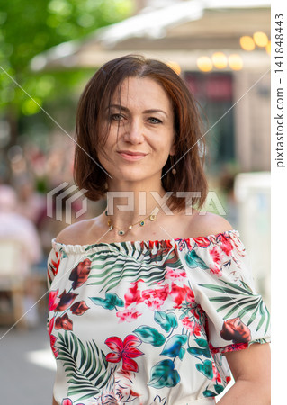Confident brunette woman with windblown hair posing outdoors in floral blouse Confident brunette woman with windblown hair posing outdoors in floral blouse 141848443