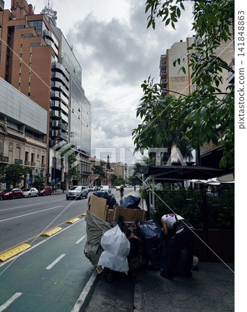 Cordoba, Argentina - April 13, 2026: Bagged waste and cardboard beside urban bicycle lane Cordoba, Argentina - April 13, 2026: Bagged waste and cardboard beside urban bicycle lane 141848863