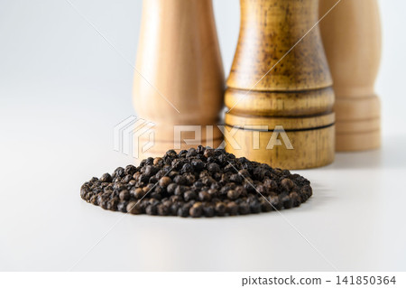 A wooden pepper mill and a kitchen utensil with rows of black peppercorns. A wooden pepper mill and a kitchen utensil with rows of black peppercorns. 141850364