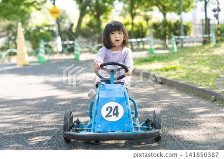 一位年輕的日本女孩在公園裡駕駛一輛藍色卡丁車，臉上洋溢著笑容。 141850387