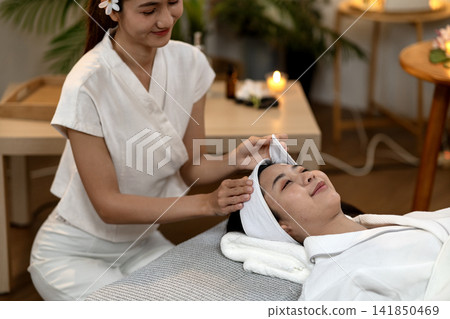Asian spa therapist performs gentle facial treatment on adult woman promoting deep relaxation healthy skin wellness serene professional setting Asian spa therapist performs gentle facial treatment on adult woman promoting deep relaxation healthy skin wellness serene professional setting 141850469